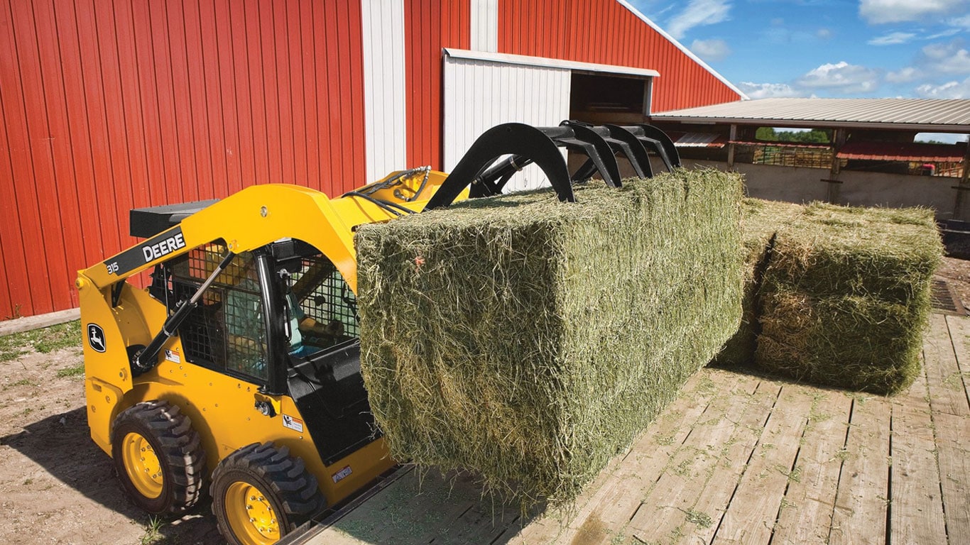 John Deere Skid Steer with Scrap Grapple Attachment picking up straw bale.